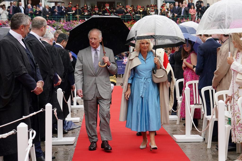 King Charles III and Queen Camilla, under umbrellas, hastily walking down a red carpet due to a security scare at a royal event in St Helier.