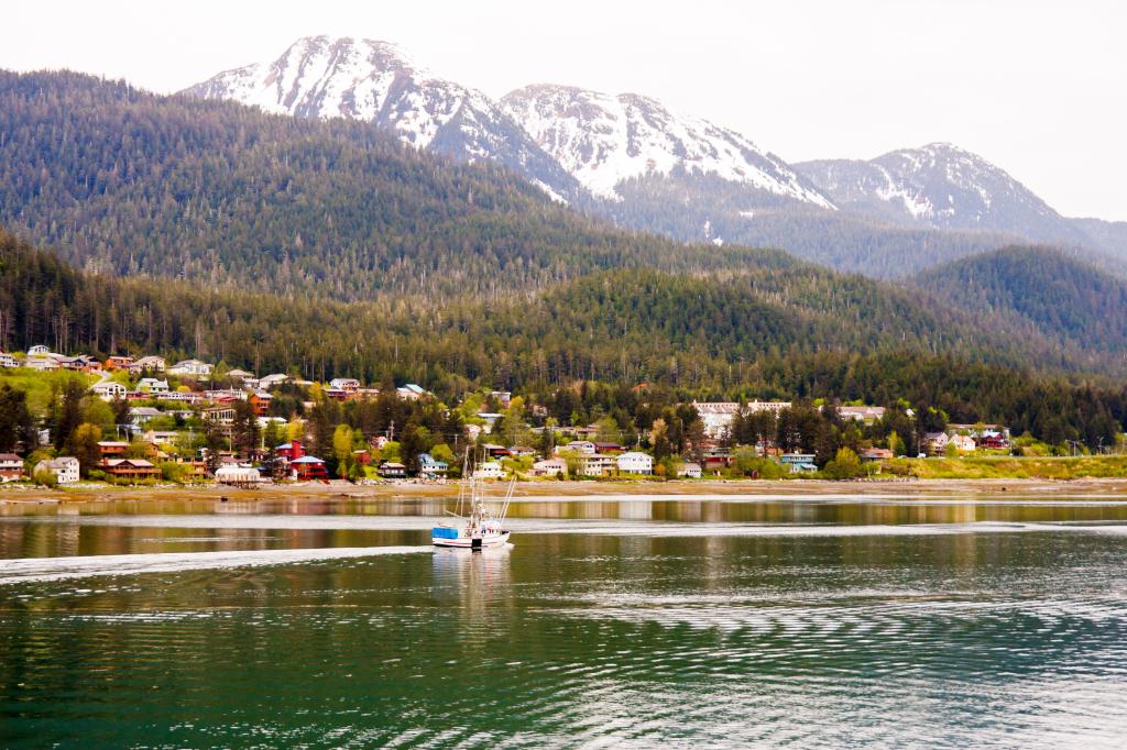 A commercial fishing boat cruising past colorful coastal homes in Alaska 