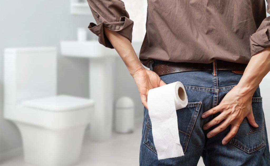 man holding toilet tissue roll in bathroom looking at loo