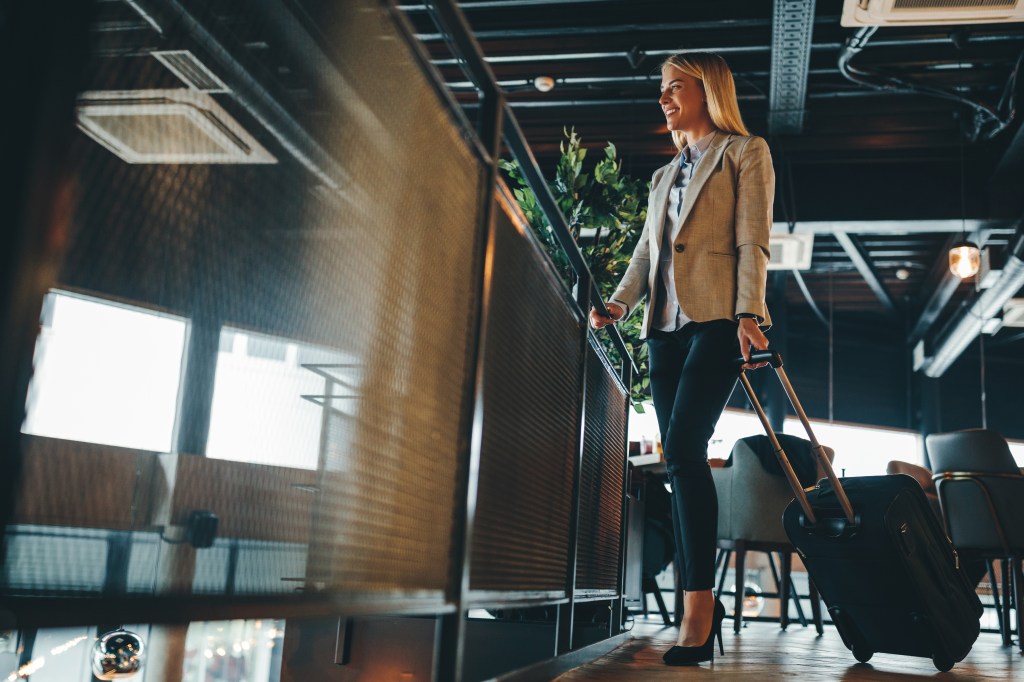 Young businesswoman holding a suitcase in a hallway, ready for a trip