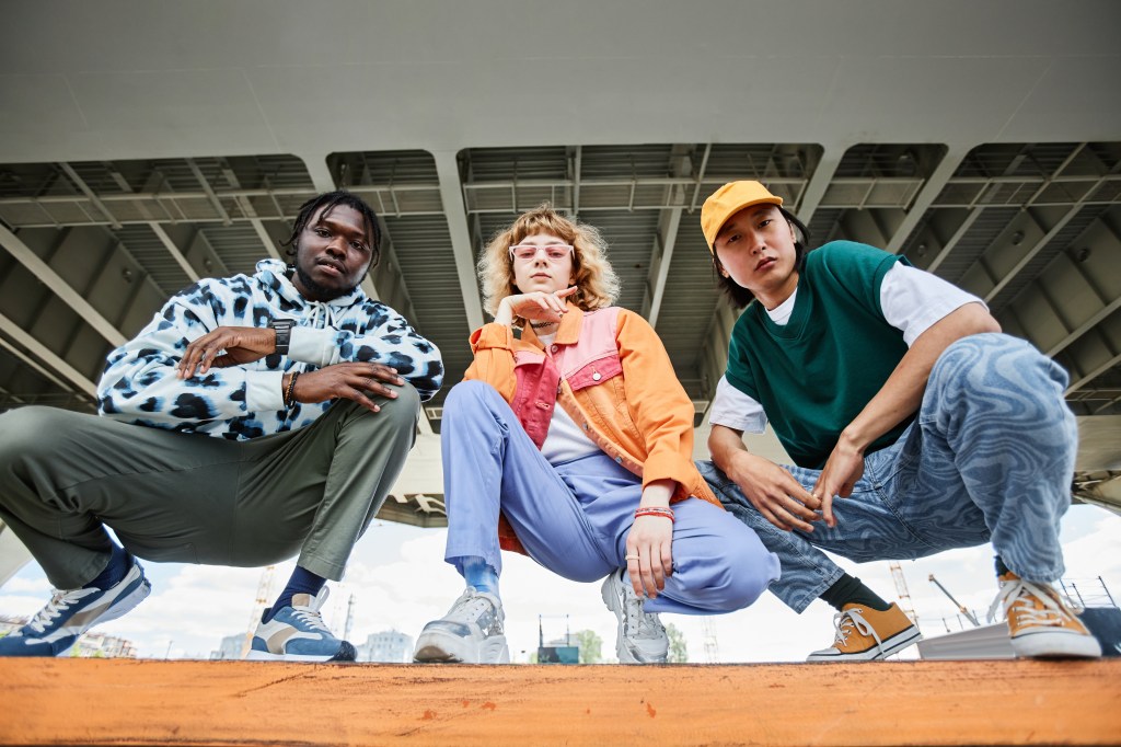 Three young people in street style clothes posing on urban stairway