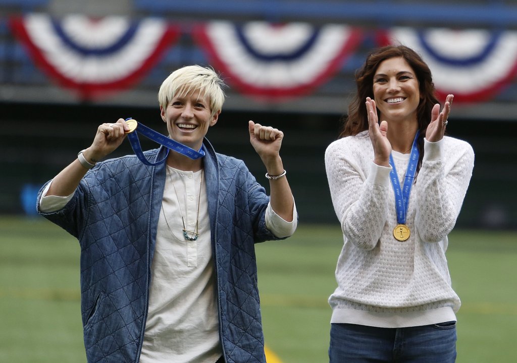 Megan Rapinoe holds up her championship medal alongside teammate Hope Solo during a homecoming ceremony before the soccer match between Seattle Reign and the Western New York Flash at Memorial Stadium, Saturday, July 11, 2015, in Seattle. 