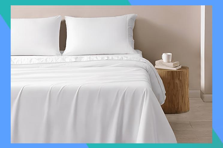 A bed with white sheets and a coffee cup on a table