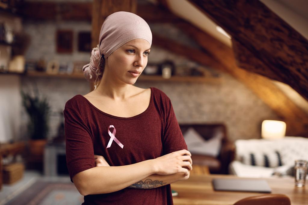 Pensive woman with cancer wearing a pink ribbon on her shirt at home