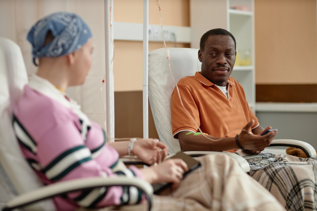 Black adult man conversing with another patient during chemotherapy treatment at a clinic