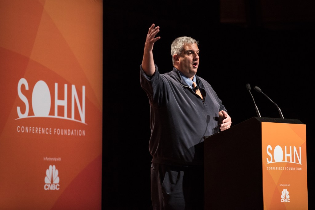 Larry Robbins, CEO of Glenview Capital Management, speaking at the 23rd annual Sohn Investment Conference, with his hand raised.