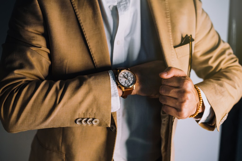 A stylish businessman in a casual suit, focusing on his watch and suit button