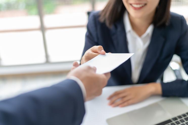 Young Asian businesswoman happily receiving a piece of paper, possibly a salary or bonus, from her manager in an office setting