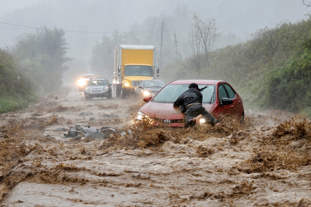 car stuck in road in mud with man pushing it out during storm