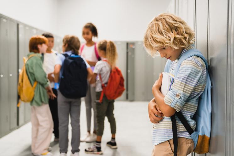 Sad schoolboy crying in a hallway, surrounded by ignoring classmates, depicting social exclusion and bullying