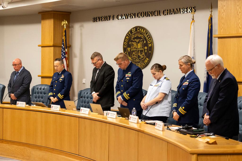 Investigative board members standing in a row during a moment of silence at the Coast Guard hearing on the Titanic experimental submersible implosion