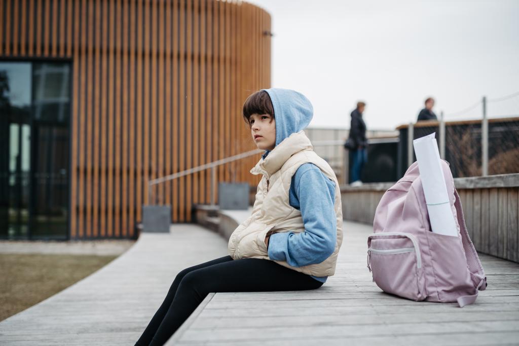 Child sits alone outside with backpack