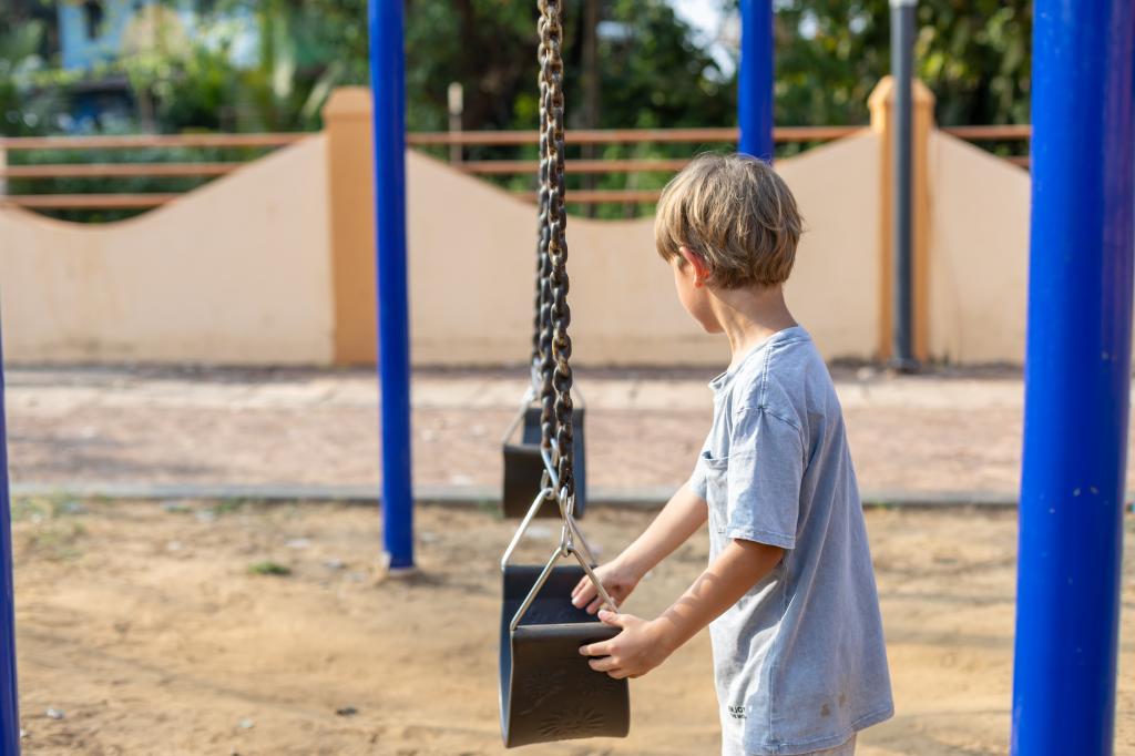 Preschooler boy standing thoughtfully near a swing on a summer day, contemplating whether to play on it during outdoor activities