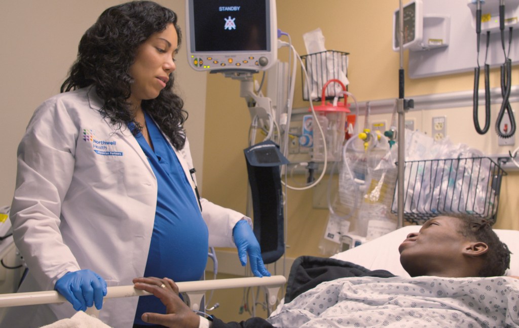 Dr. Mirtha Macri in a white coat standing next to a man in a hospital bed in episode 102 of Lenox Hill