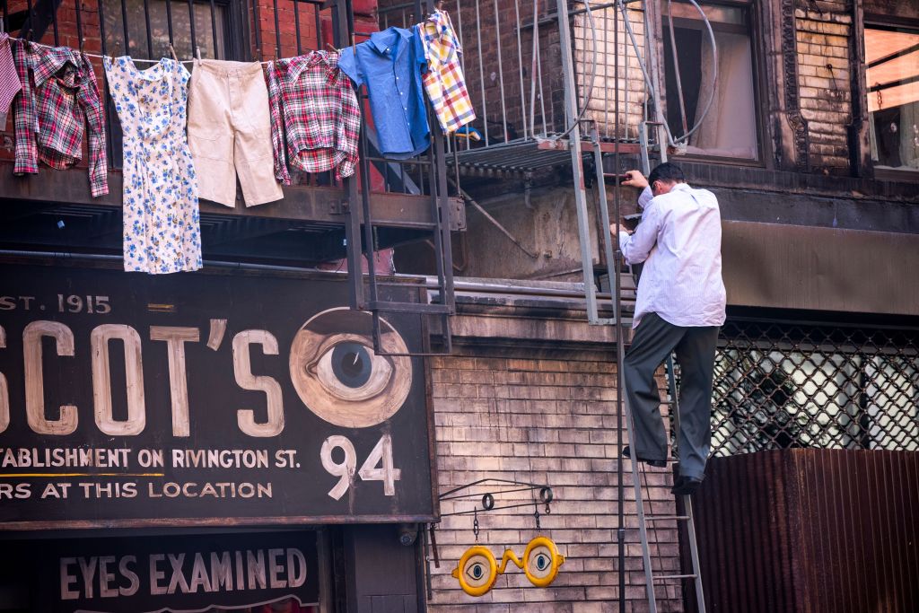 Timothee Chalamet climbs a ladder outside the Moscot store on the set of "Marty Supreme." 