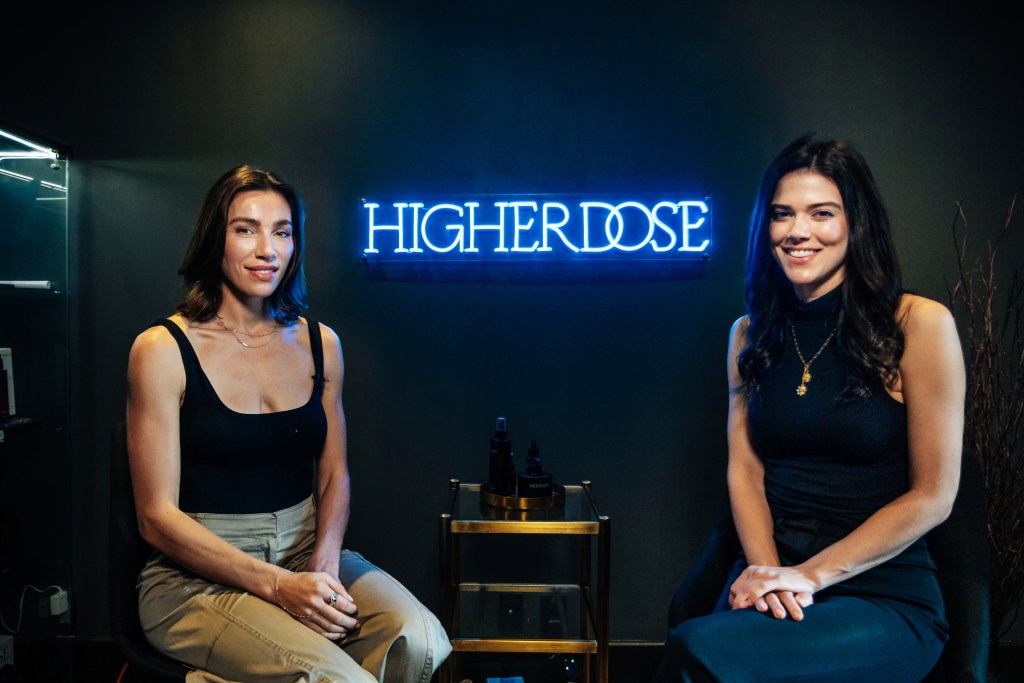 Co-Founder of Higher Dose, Lauren Berlingeri, and Lydia Moynihan sitting in front of a neon sign at the Howard Hotel in Manhattan, photographed by Emmy Park in 2024.