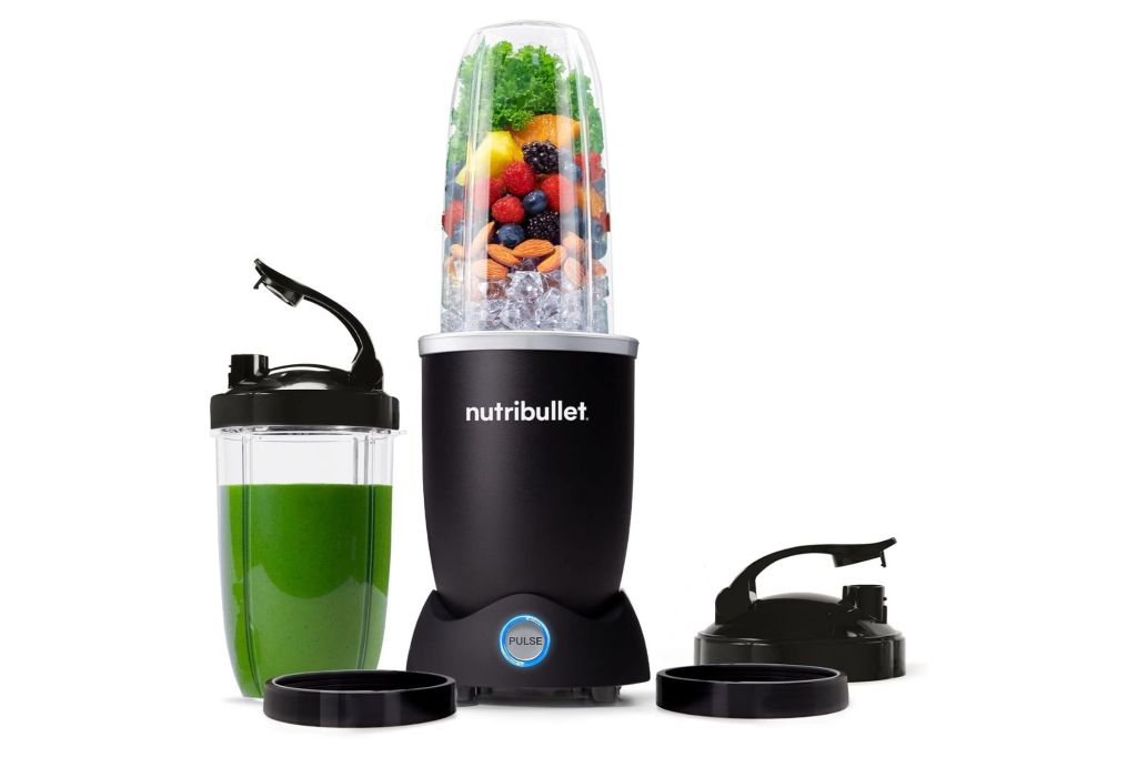 A nutribullet blender with fruit and a plastic cup with a green drink.