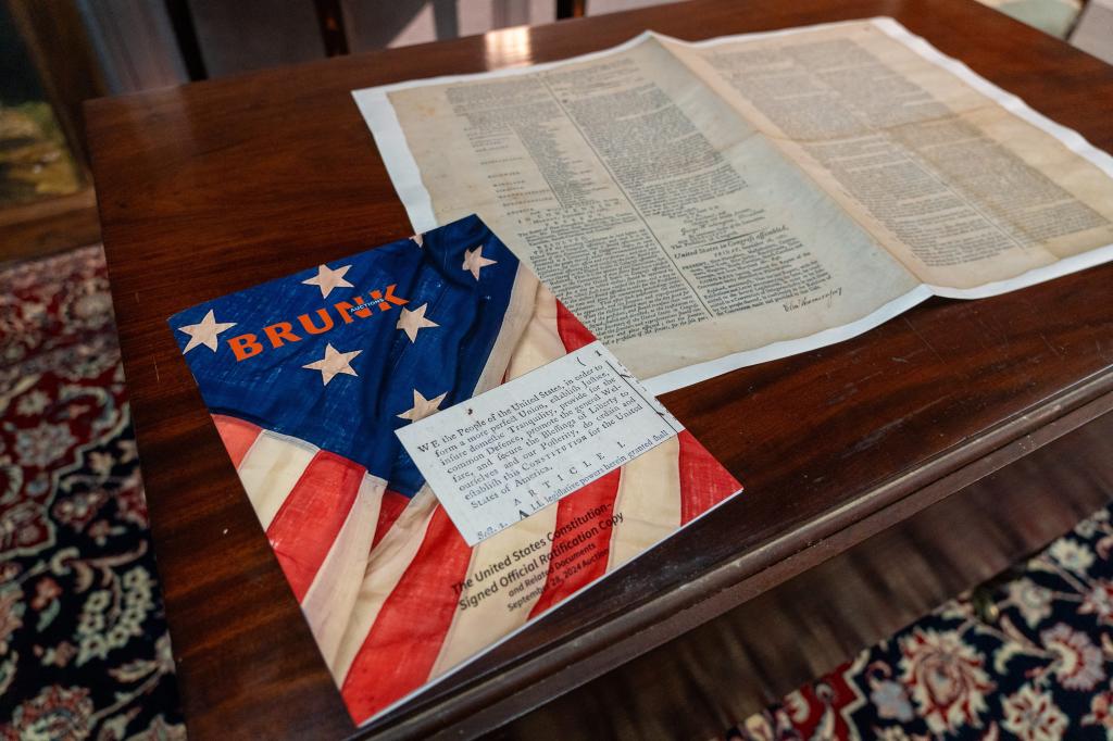 An auction booklet next to a facemile of a signed official ratification copy of the United States Constitution by Brunk Auction.