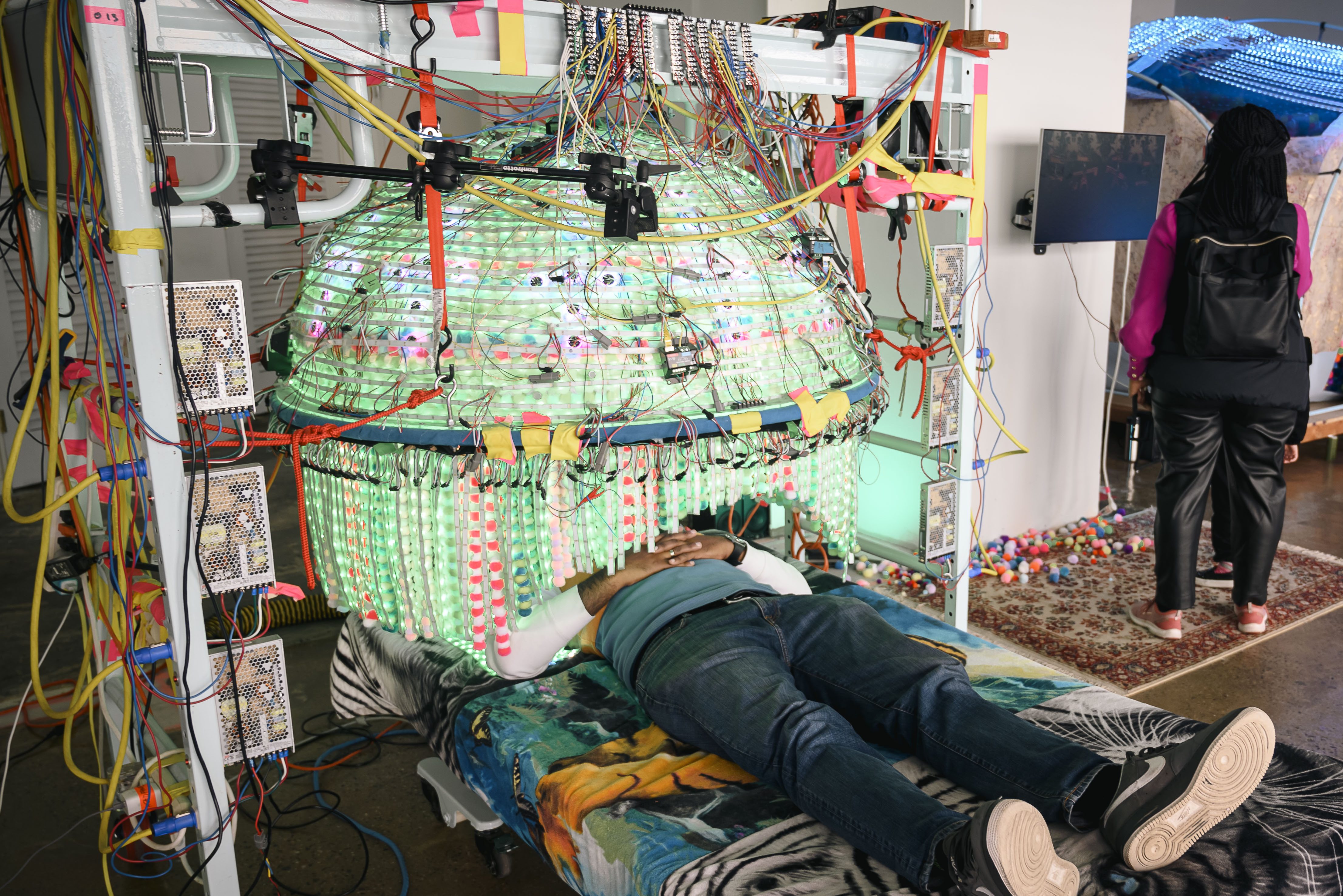 A visitor reclines on a bed and looks upward into a chandelier-like fixture.