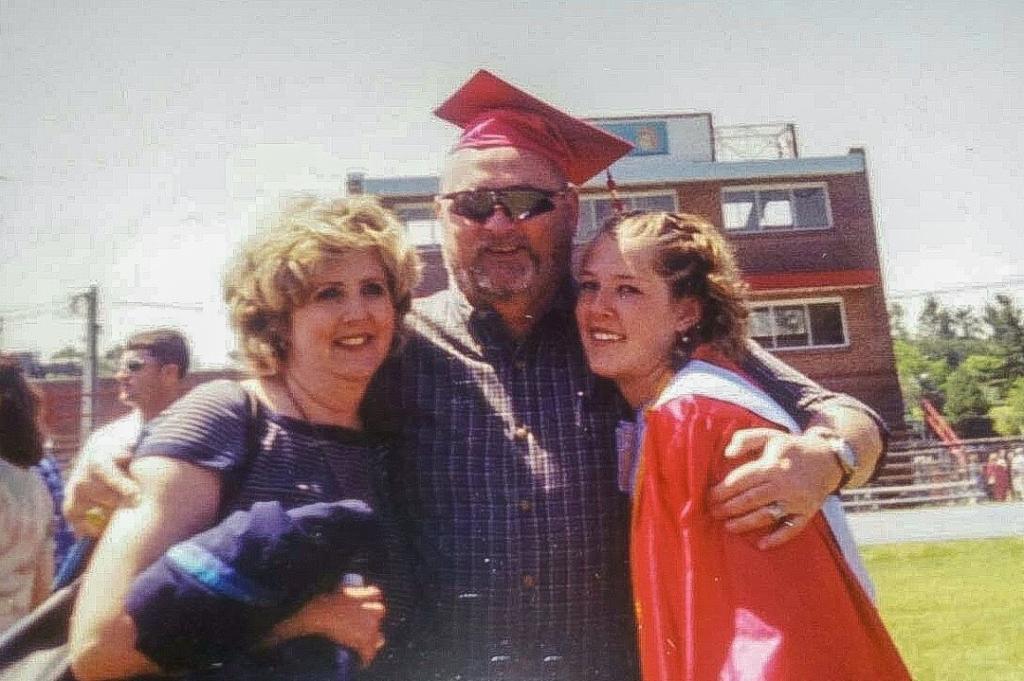 Lauren Sisler in her high-school graduation robe, as her dad hugs Lauren and her mom