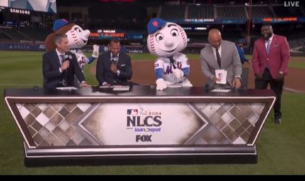 Derek Jeter start to get up from the desk during the Fox Sports broadcast as Mr. Met sits next to him.