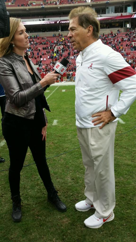 Sisler holding a microphone toward former University of Alabama football coach Nick Saban, on a football field