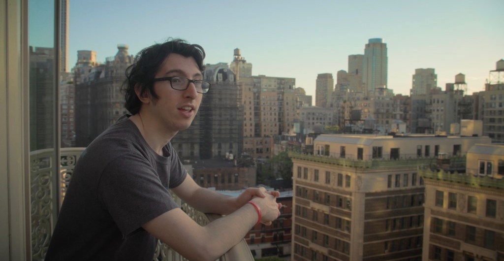 Weiner, whose father co-created the kid's show "Dora the Explorer," seen here in a shot from his own film leaning over a rail while on a rooftop looking off to hisright with part of the skyline behind him, the film is  a mockumentary titled "Citizen Weiner," about his run for City Council.