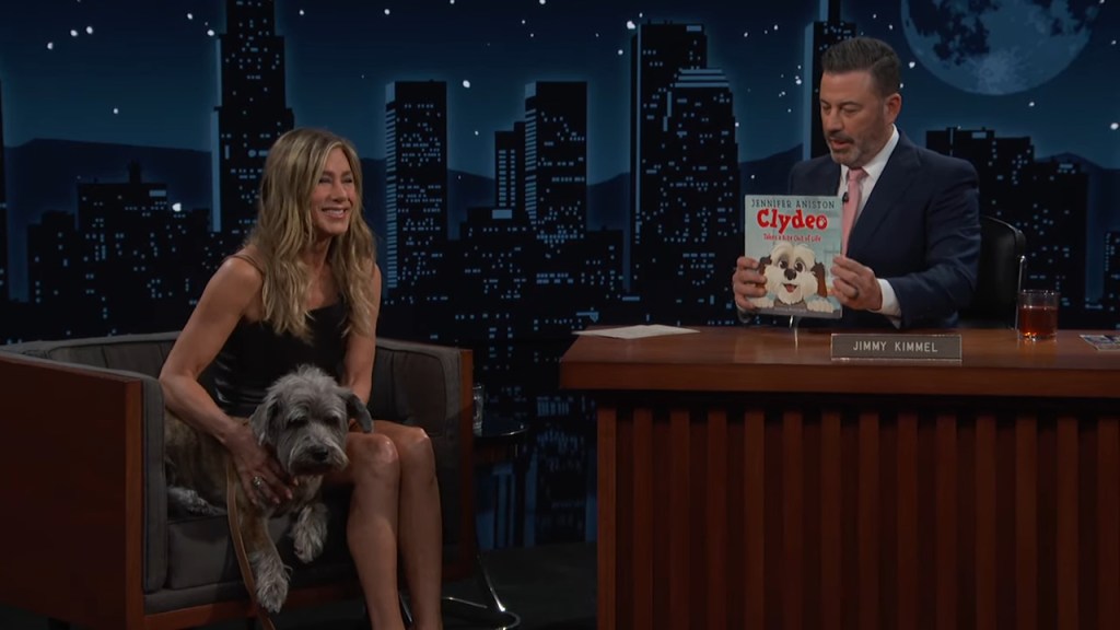 Jennifer Aniston sitting on a chair with her dog Clyde on her lap during a talk show