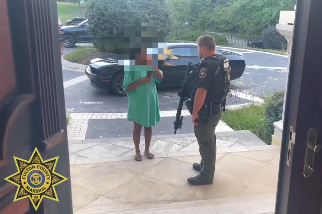 A woman with a blurred face speaks to an officer with a long gun.