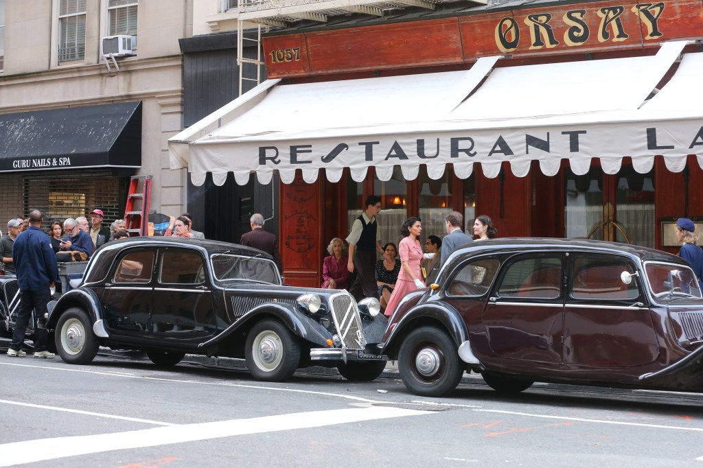 Exterior Orsay restaurant with 1950s cars parked in front for "Marty Supreme." 