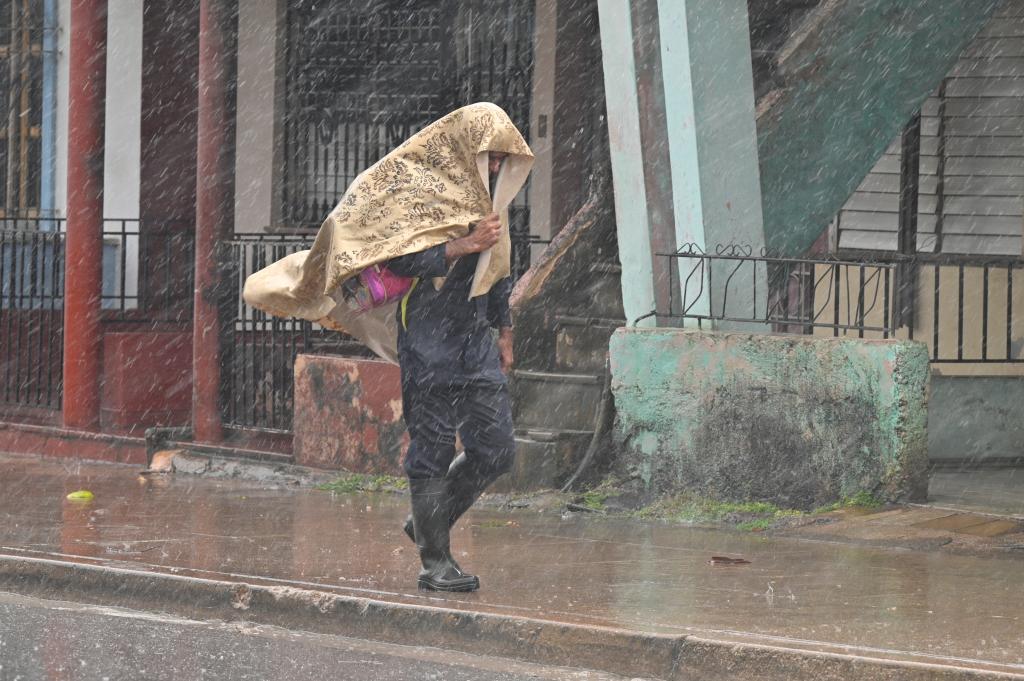 A man protects his head from the rain as he walks down a street after Hurricane Rafael made landfall on Cuba.