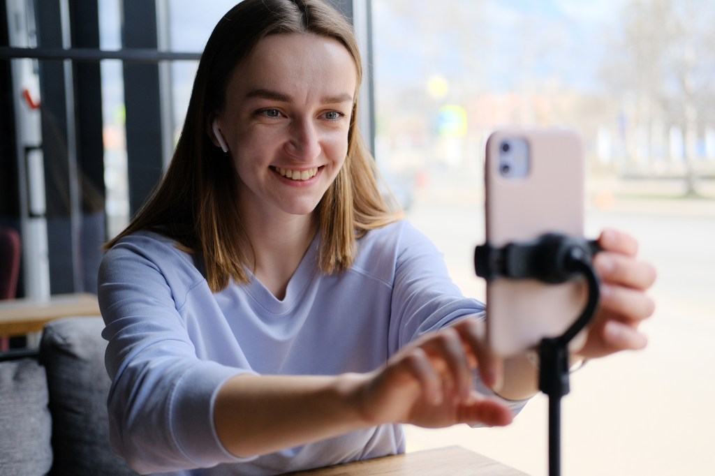 Young woman using smartphone to record live video for her blog in a cozy cafe