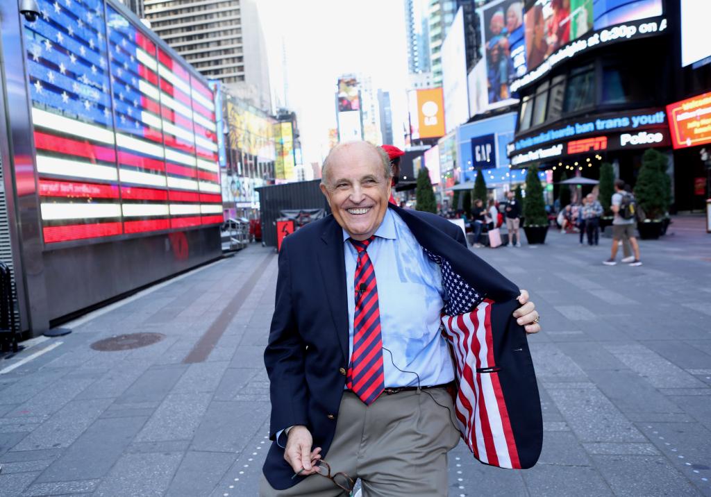 Giuliani standing in Times Square with an open blazer that has the American flag sewn on the inside of his coat.