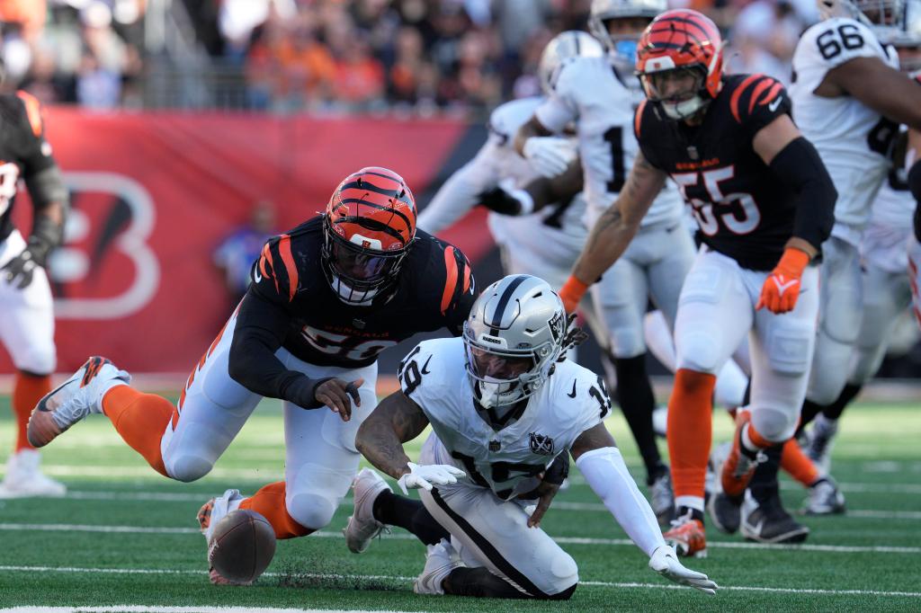 Raiders wide receiver DJ Turner attempting to recover a fumble while being closely watched by Bengals player Joseph Ossai during an NFL game.