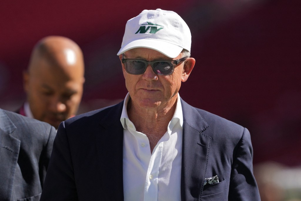 New York Jets owner Woody Johnson in a white hat and suit walking on the field before the game against the San Francisco 49ers at Levi's Stadium