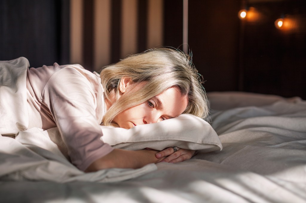 Middle-aged woman looking unhappy and tired, lying in bed at home.