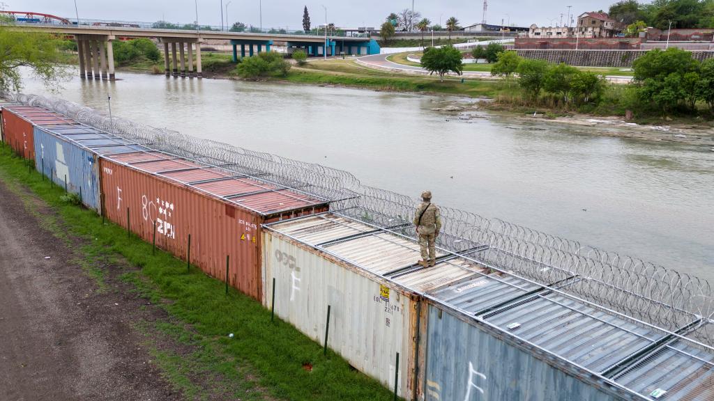 A lone soldier stands atop a wall of shipping containers erected by the state of Texas.