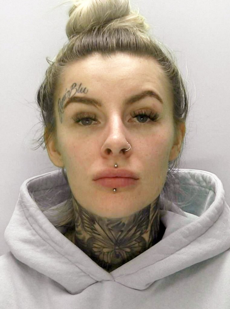 Blonde woman in grey hoodie with tattoos and facial piercings looking directly at the camera in her mugshot