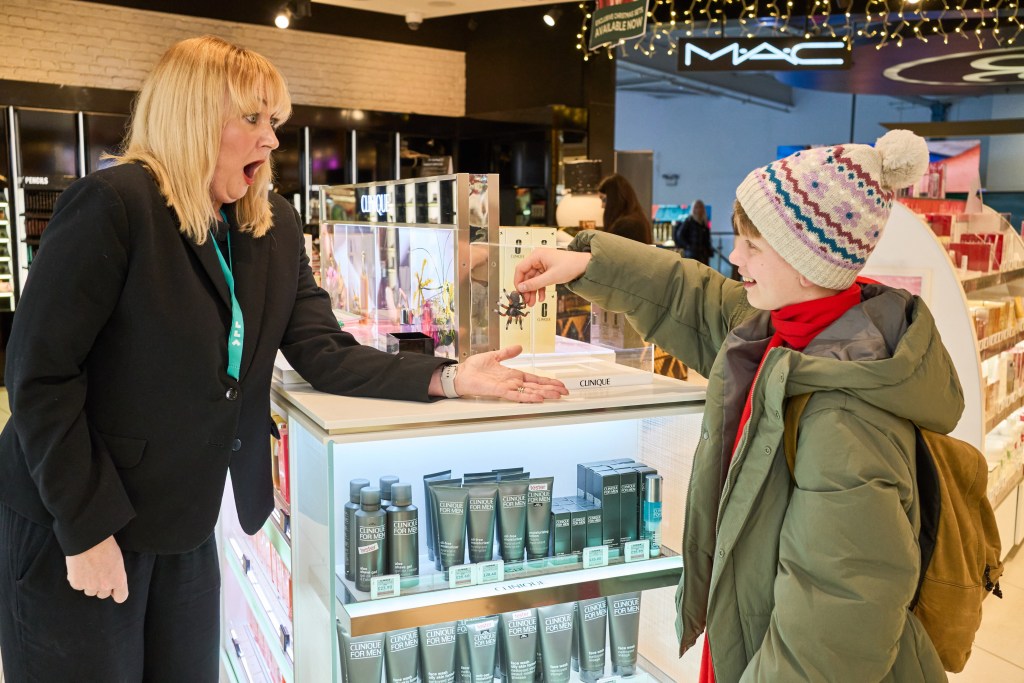 Actor Tom Mandrake hands a fake tarantula to a retail employee at London Luton Airport, recreating an iconic scene from Home Alone.