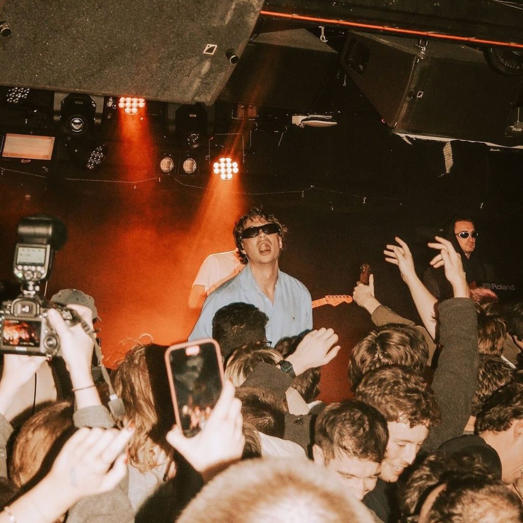 Man in sunglasses performing on stage at Goldfield Trading Post, crowd watching in the background