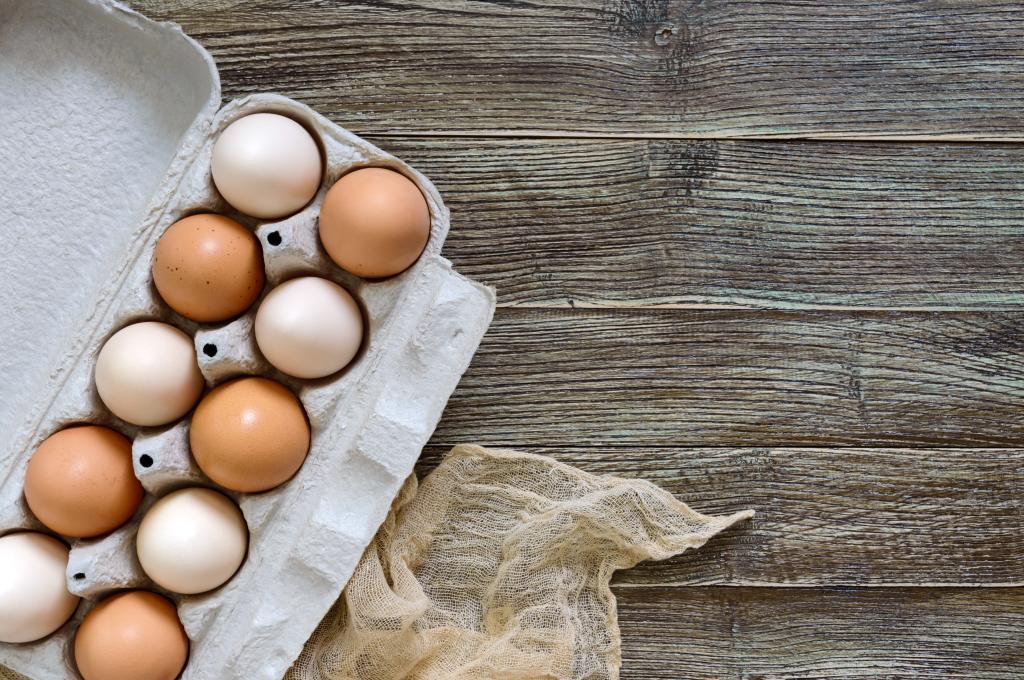 Top view of fresh raw brown and white chicken eggs in carton box on a wooden background