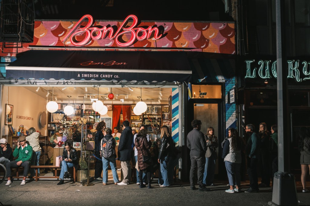 A group of people standing in a long line outside the BonBon candy store in Manhattan, New York at night.