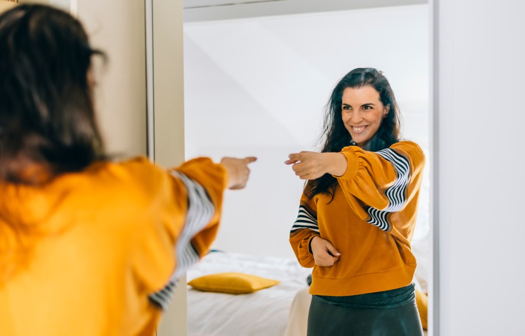 There's still time to change your mindset from fixed to growth. Here, a woman wearing a golden-colored sweatshirt points at herself in the mirror.