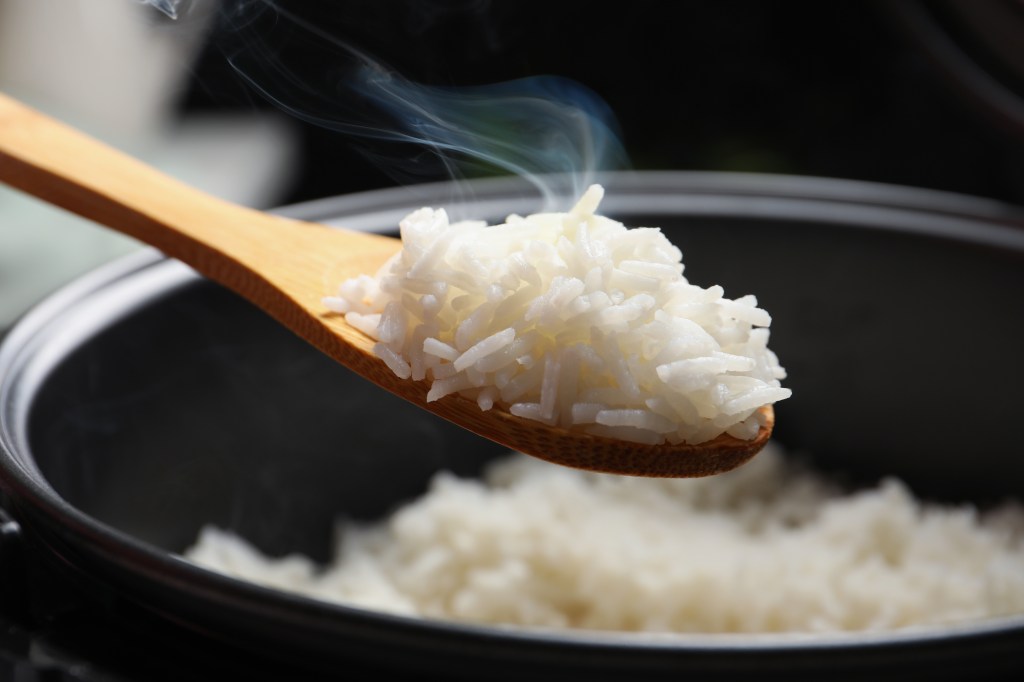 Closeup of a wooden spoon with hot, tasty rice over a cooker