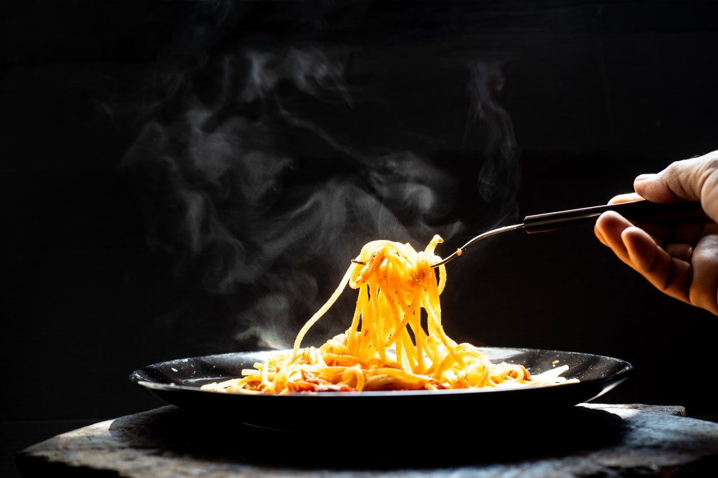 The steam from hand holding Spaghetti on a fork. Pasta with fresh tomatoes and herbs