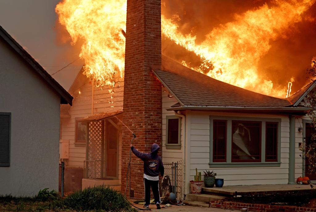 A person uses a garden hose in an effort to save a neighboring home from catching fire in LA County.