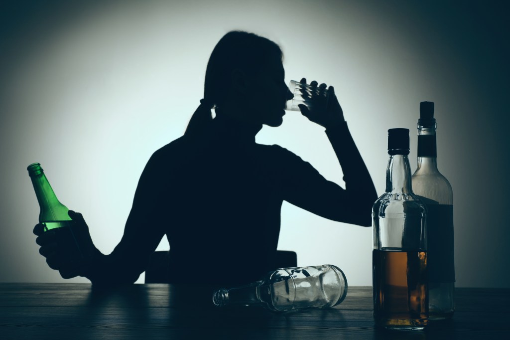 Silhouette of a woman drinking beer on a wooden table, illustrating alcohol addiction