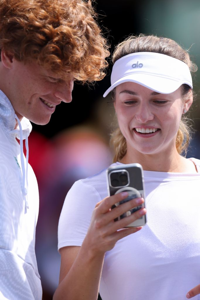 Jannik Sinner and Anna Kalinskaya reviewing a strategy on a cellphone during a practice session at the 2024 Wimbledon Championships