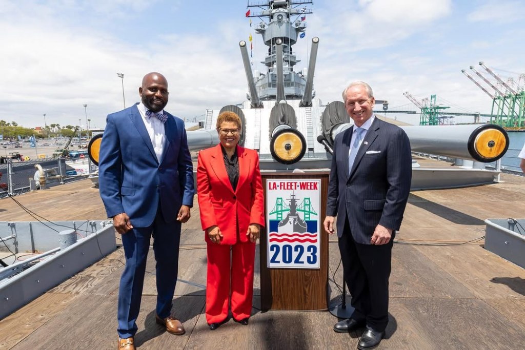 Brian Williams, Karen Bass and another man standing in front of a naval ship by an LA Fleet Week 2023 sign.