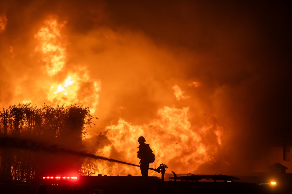  A firefighter stands on top of a fire truck to battle the Palisades Fire as it burns homes.